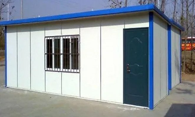 Single-storey prefab shelter with white sandwich-panel walls, steel door and window grille